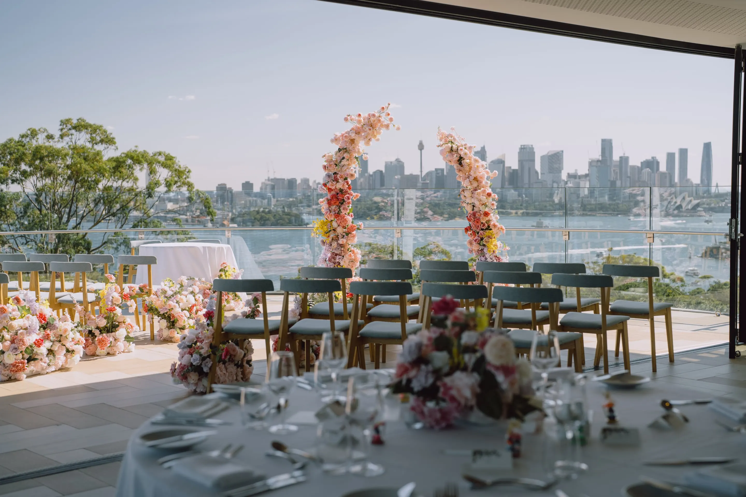 Reception tables set with pastel florals on a terrace overlooking Sydney Harbour and the city