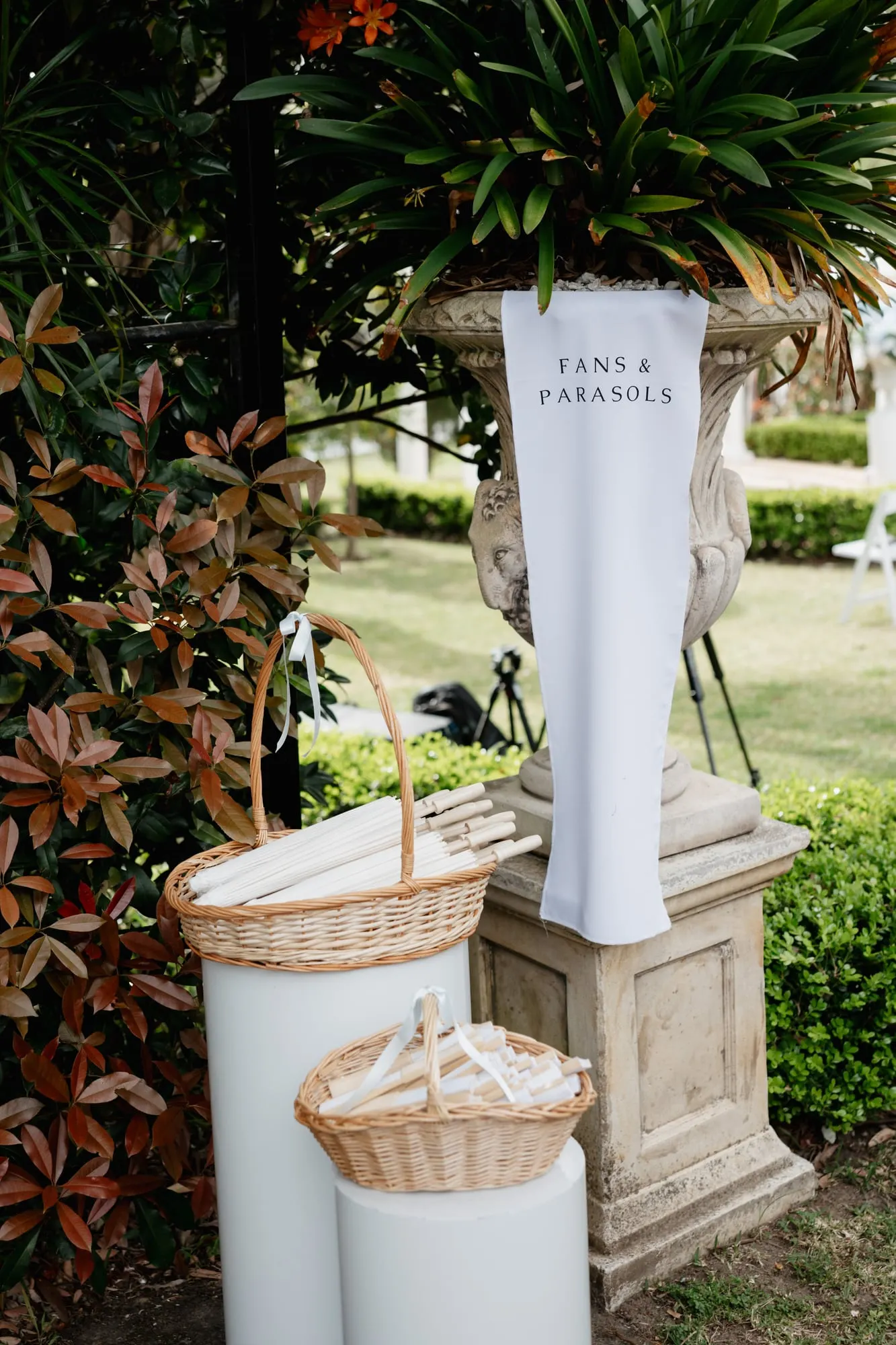 Parasols and paper fans in baskets at the ceremony entrance, beside a welcome sign