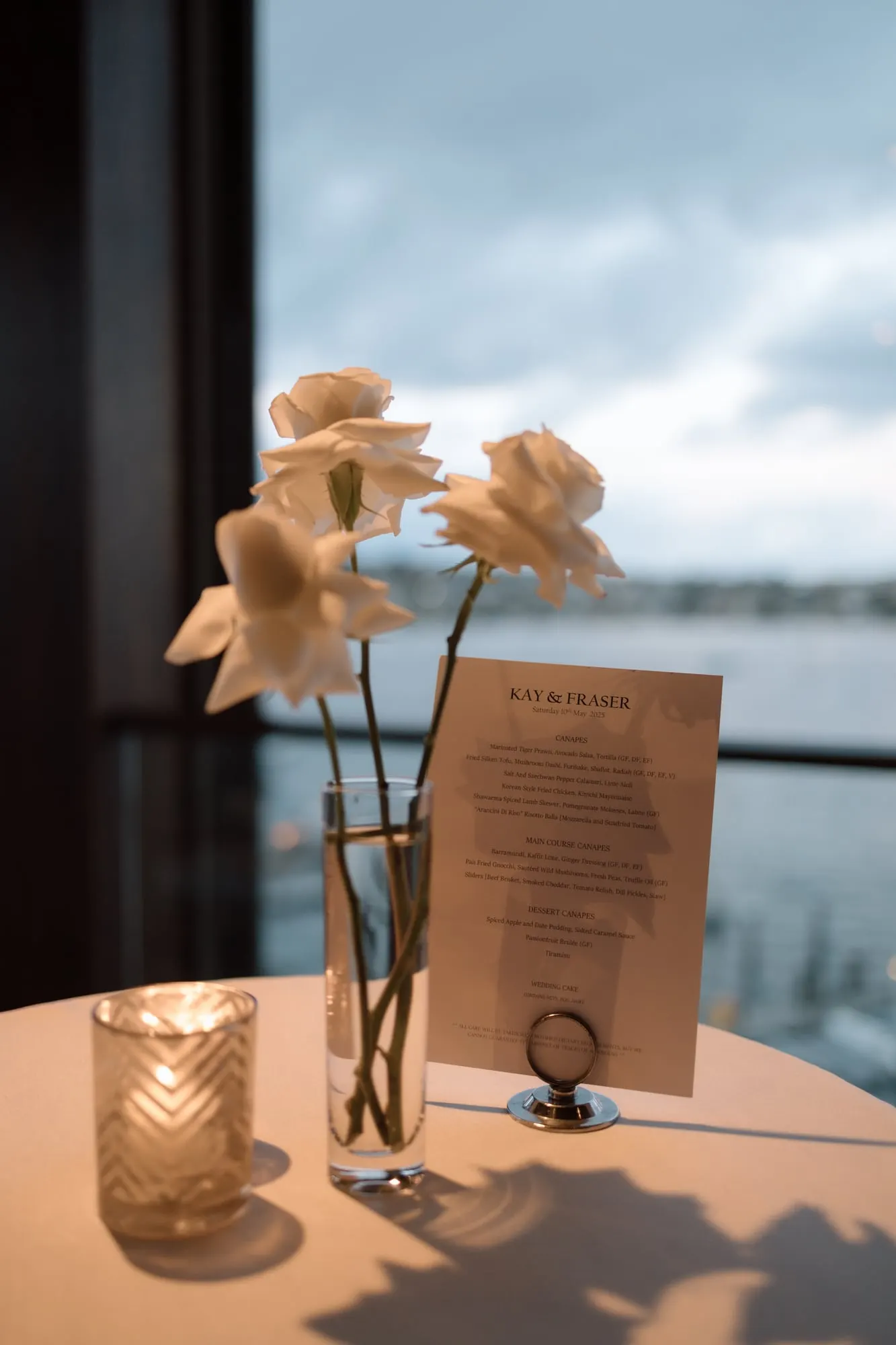 Bud vases with peach roses on a table by a window overlooking the water